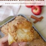 Hand holding an Apple Crisp Sourdough Cinnamon Roll over a 9x13 pan.