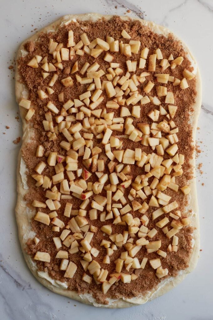 Diced apples added on to of spiced sugar mixture for apple crisp sourdough cinnamon rolls.