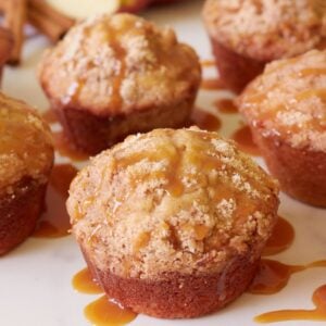 Sourdough apple muffins with a caramel drizzle next to an apple cut in half and cinnamon sticks.