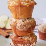 Three sourdough apple muffins stacked on top of each other with half an apple and cinnamon sticks in the background.
