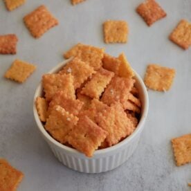 Small white bowl filled with sourdough cheez it crackers with more crackers scattered around the bowl.