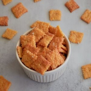 Small white bowl filled with sourdough cheez it crackers with more crackers scattered around the bowl.