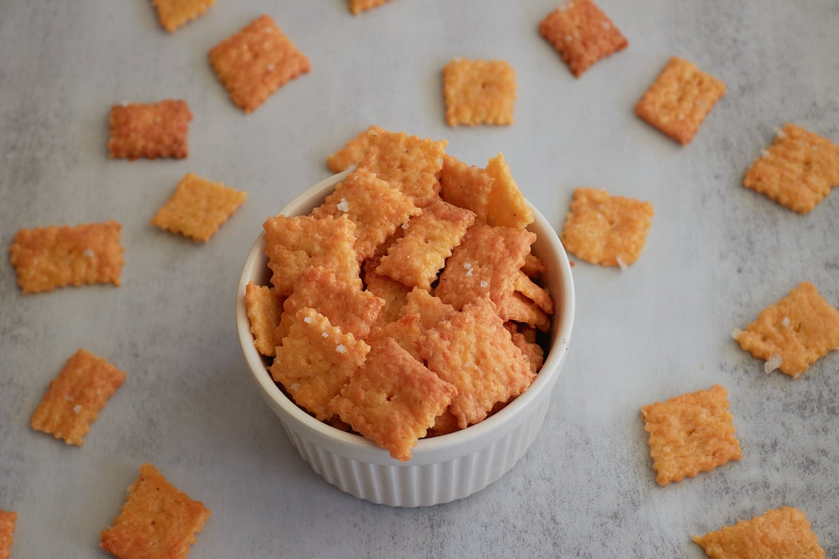 Small white bowl filled with sourdough cheez it crackers with more crackers scattered around the bowl.