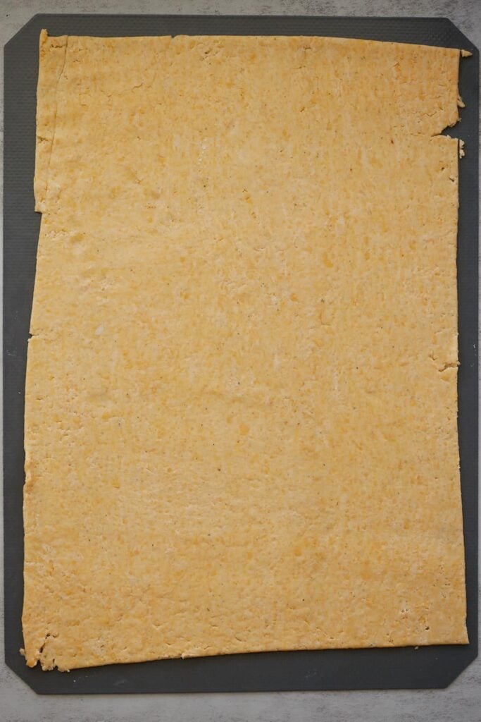 Sourdough Cheez It Cracker dough rolled out 1/8 inch on a silicone mat.