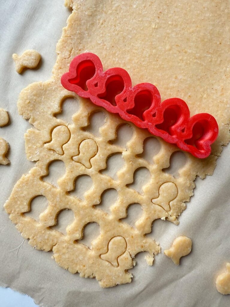 Cutting out fish shaped crackers in sourdough goldfish dough using a small fish cut out.
