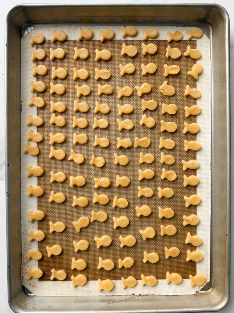 Fish-shaped sourdough goldfish dough placed on a sheet pan lined with a silicone mat.