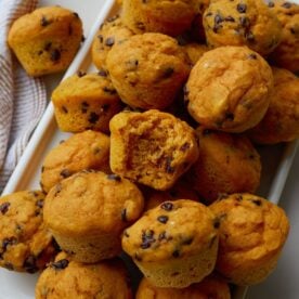 White plate full of sourdough pumpkin mini muffins next to a brown and white cloth napkin.