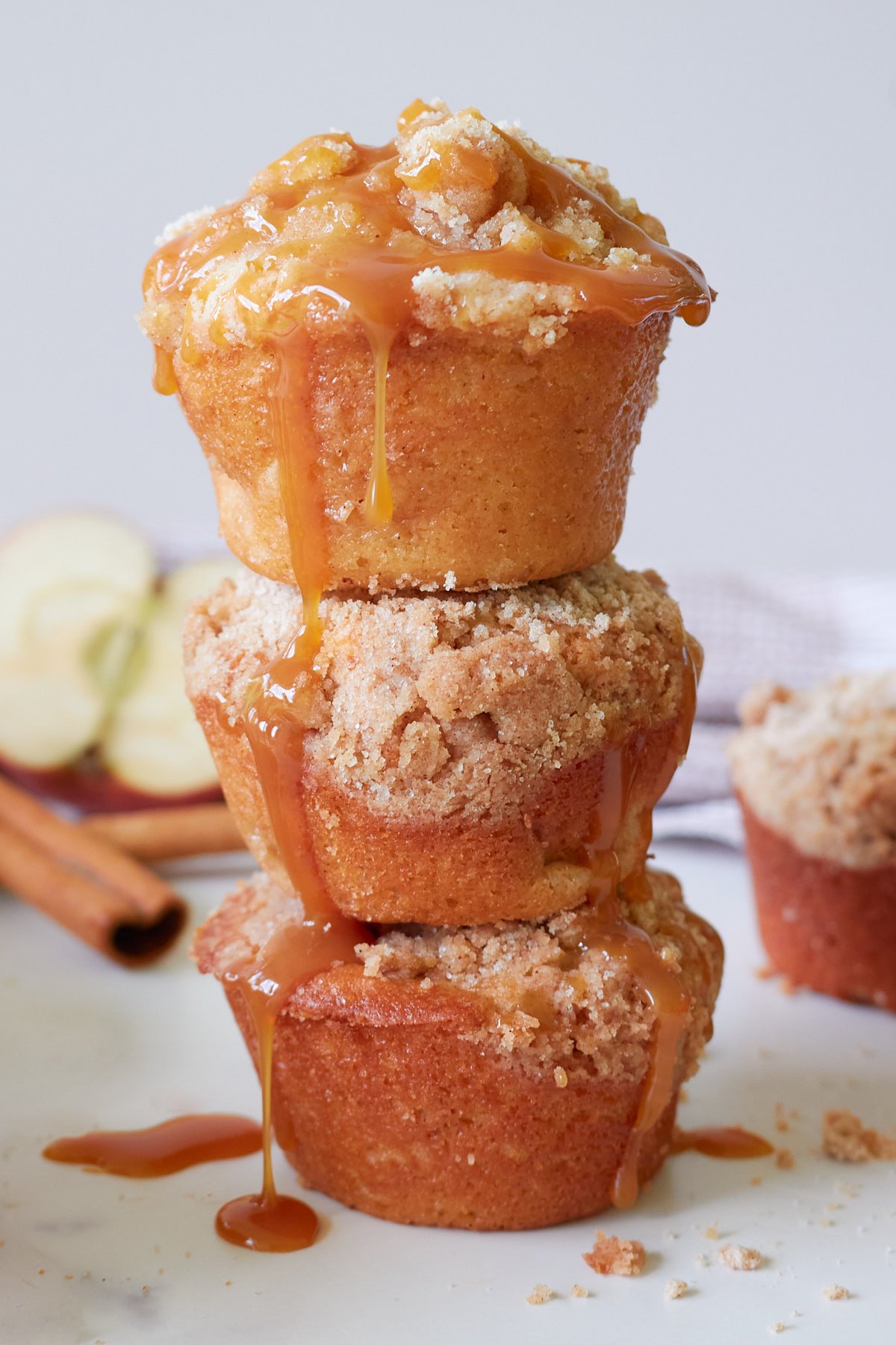 Three sourdough apple muffins stacked on top of each other with half an apple and cinnamon sticks in the background.