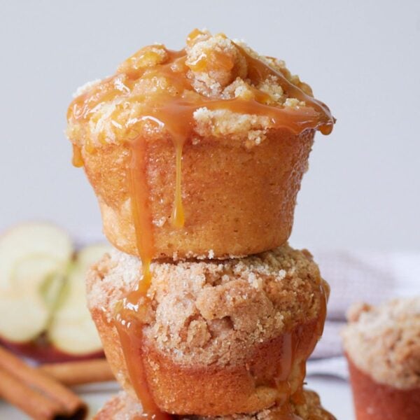 Two sourdough apple muffins stacked on top of each other with half an apple and cinnamon sticks in the background.