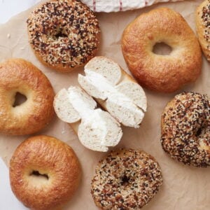 Sourdough Bagels on brown parchment paper with one sliced in half with cream cheese.