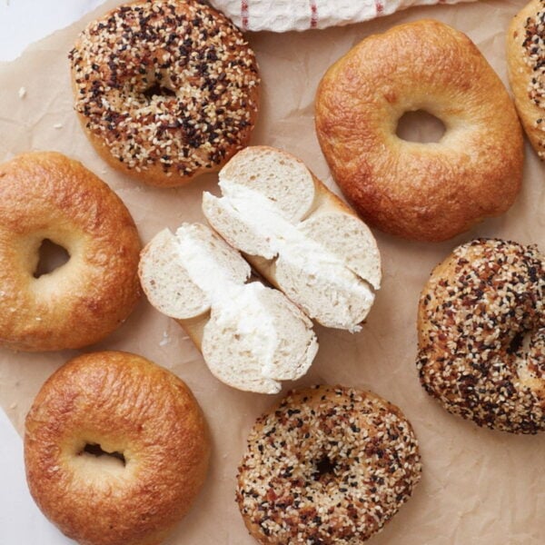 Sourdough Bagels on brown parchment paper with one sliced in half with cream cheese.