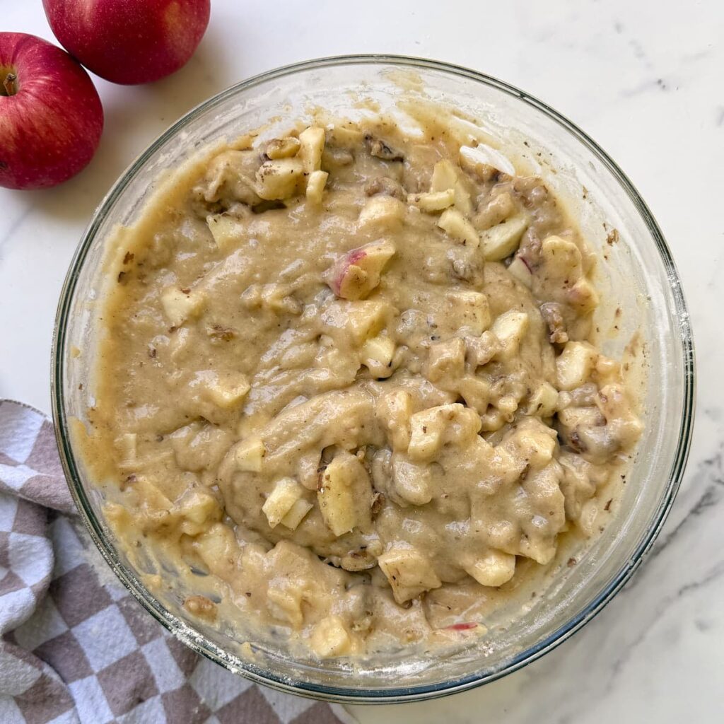 Apples and walnuts added to batter for sourdough discard apple cake in a clear bowl.