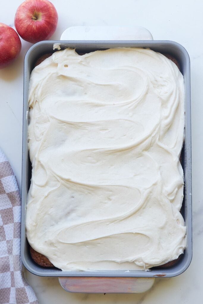 Cream cheese frosting added to sourdough discard apple cake in a 9x13 pan.
