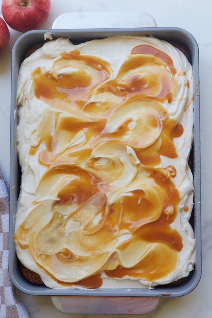Caramel topping added on top of cream cheese frosting on sourdough discard apple cake in a 9x13 pan.