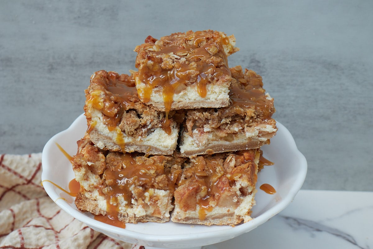 Sourdough Apple Cheesecake Bars stacked on top of each other on a white stand.