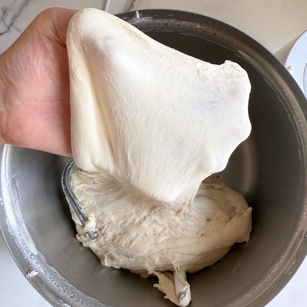 Hand pulling out a piece of dough for Sourdough Bagels to do the window test.