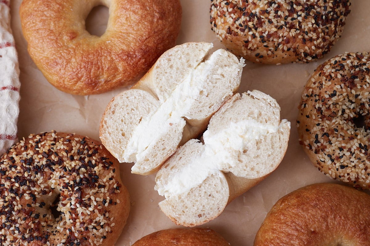 Sourdough Bagels on brown parchment paper with one sliced in half with cream cheese.