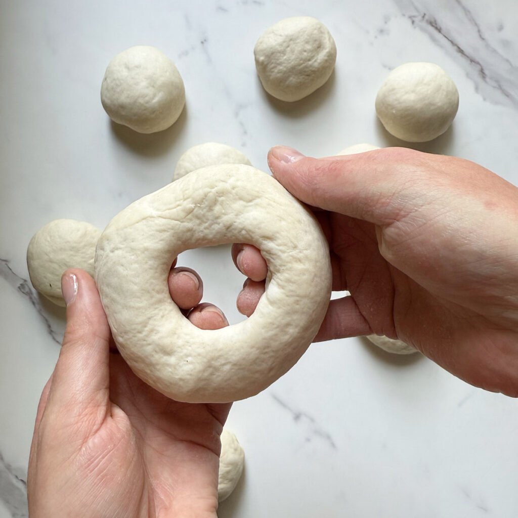 Hand holding Sourdough bagel dough shaped into a circle with a hole in the center.