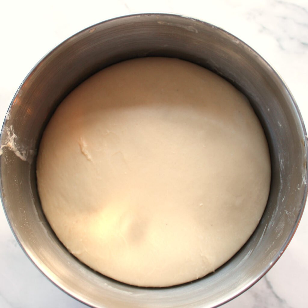 Sourdough dinner roll dough after the first rise in a metal bowl.