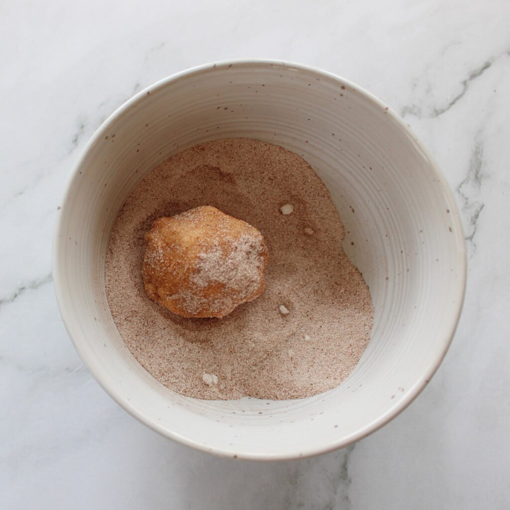 Cookie dough ball coated in cinnamon and sugar for Sourdough Pumpkin Snickerdoodles.