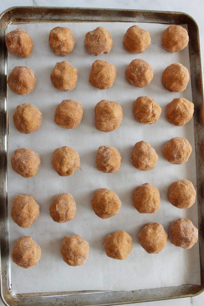 30 dough balls coated in cinnamon sugar mixture on a parchment lined sheet pan.