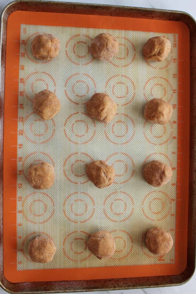 12 Sourdough Pumpkin Snickerdoodle dough balls on a baking sheet lined with a silicone baking mat.