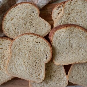 Slices of Sourdough Sandwich Bread next to each other on a wooden cutting board next to a brown and white towel.