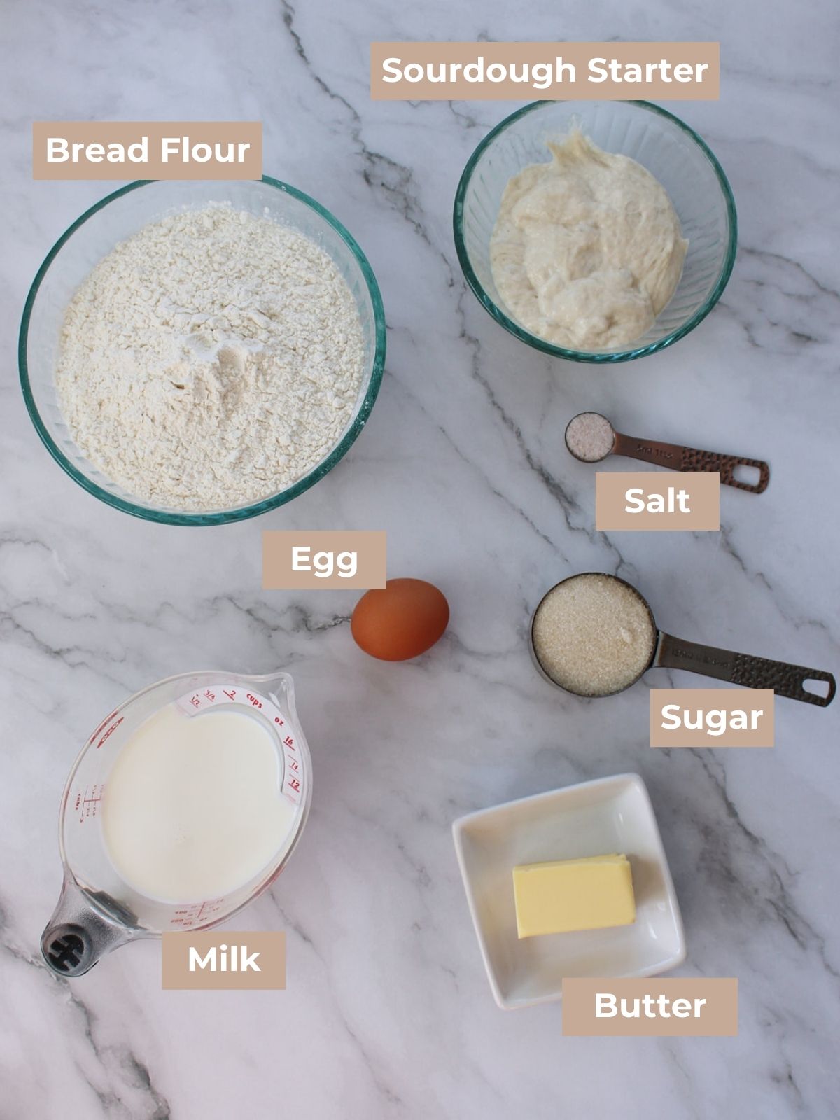 Ingredients for sourdough dinner rolls in clear bowls on a white and grey background.