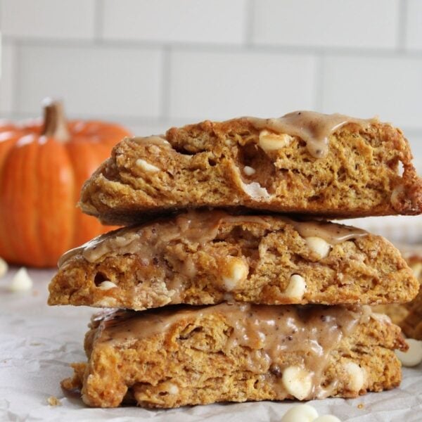 3 Sourdough pumpkin scones stacked on top of each other next to more sourdough pumpkin scones and an orange pumpkin.