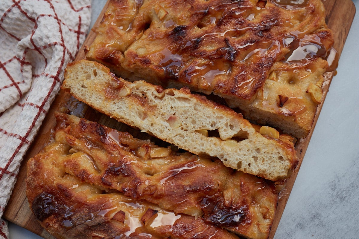 Slices of Caramel Apple Sourdough Focaccia on a wooden board next to a white and red towel.
