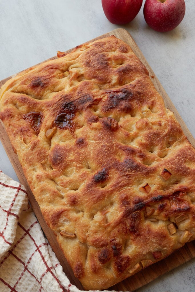 Caramel Apple Sourdough Focaccia on a wooden board next to a white and red towel.