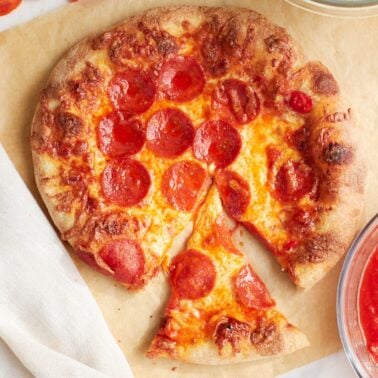 A round same day sourdough pepperoni pizza crust with a slice cut out and being pulled away.