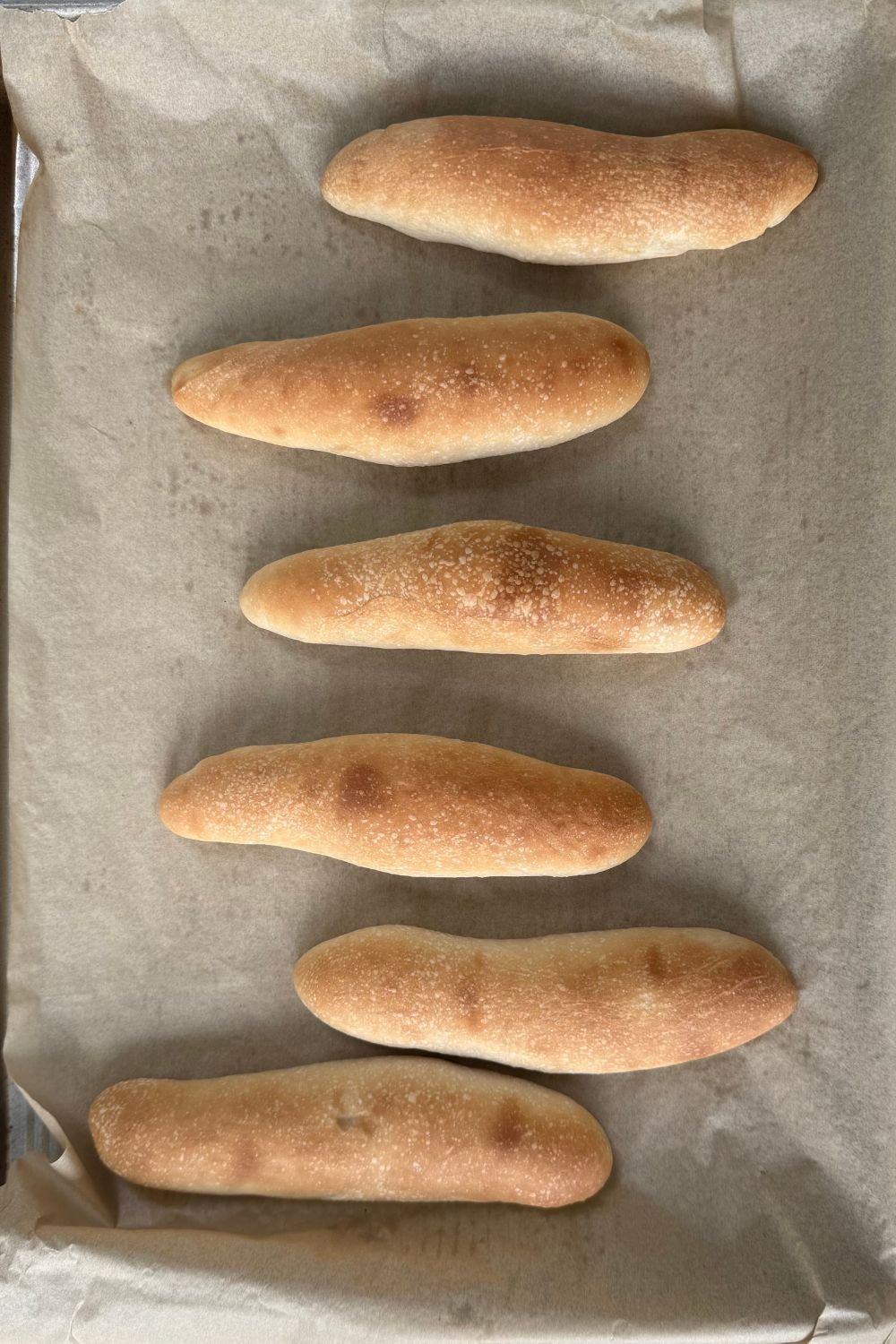 6 golden brown sourdough breadsticks baked on a parchment lined sheet pan.