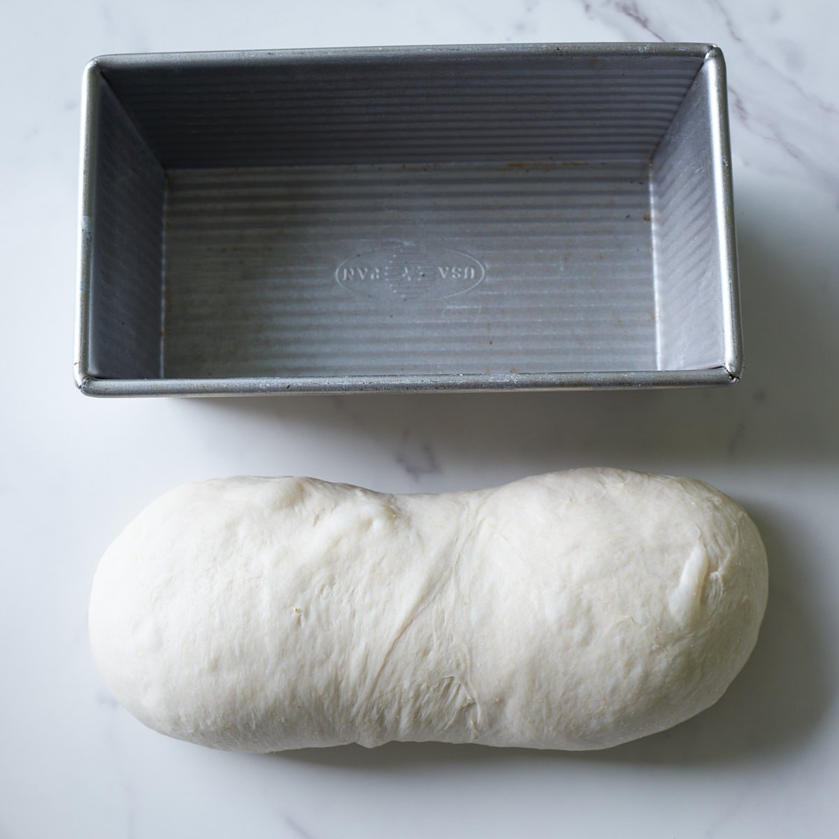 Dough for sourdough sandwich bread shaped into a long rectangle next to a loaf pan.