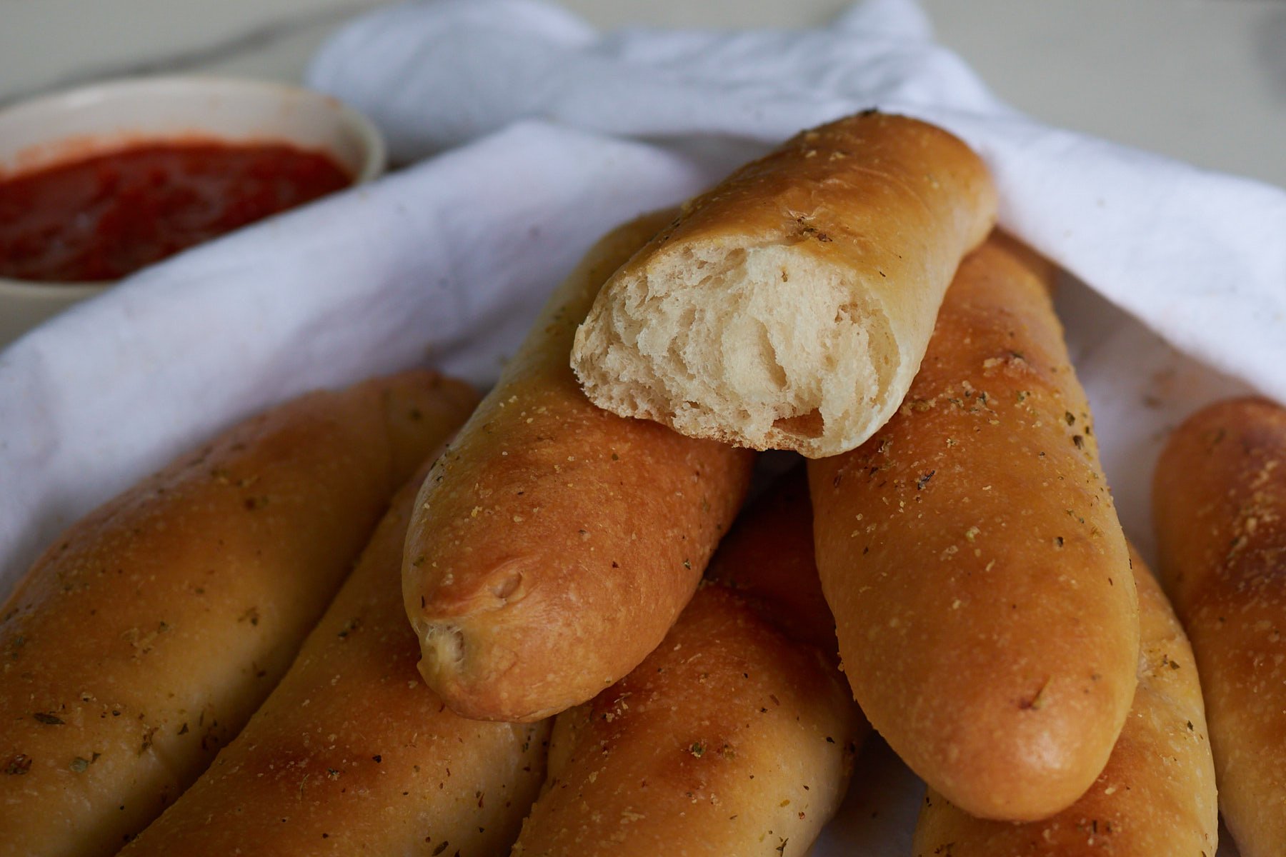 Half of a sourdough breadstick on top of a stack of golden brown sourdough breadsticks.