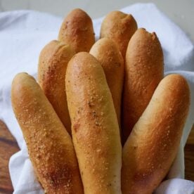 Golden brown breadsticks in a bowl lined with a white tea towel.