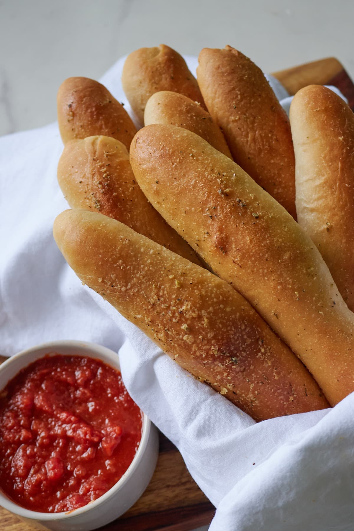 golden brown sourdough breadsticks wrapped in a white tea towel with a cup of marinara sauce next to it.