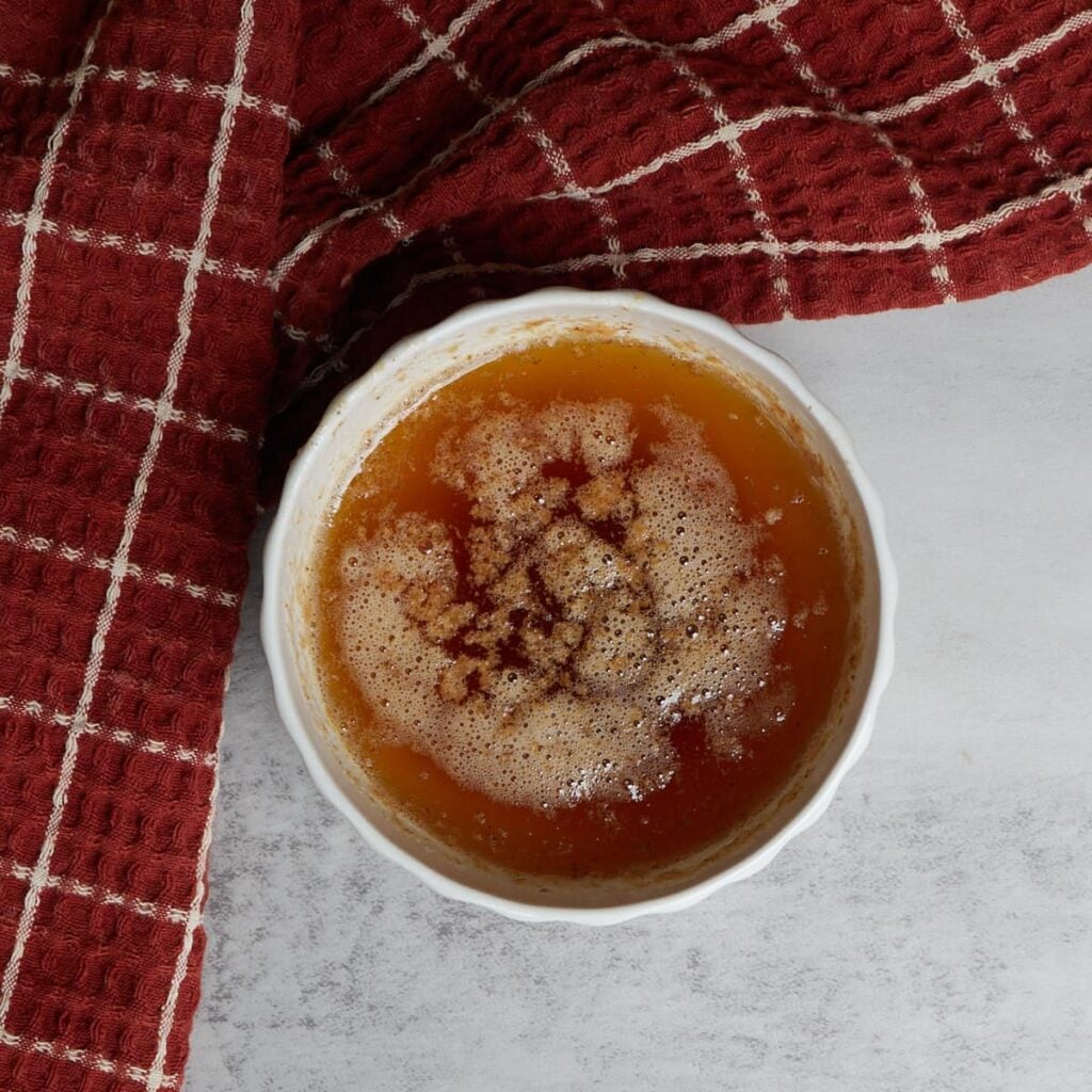 Browned butter in a white bowl with an orange and white checkered tea towel.