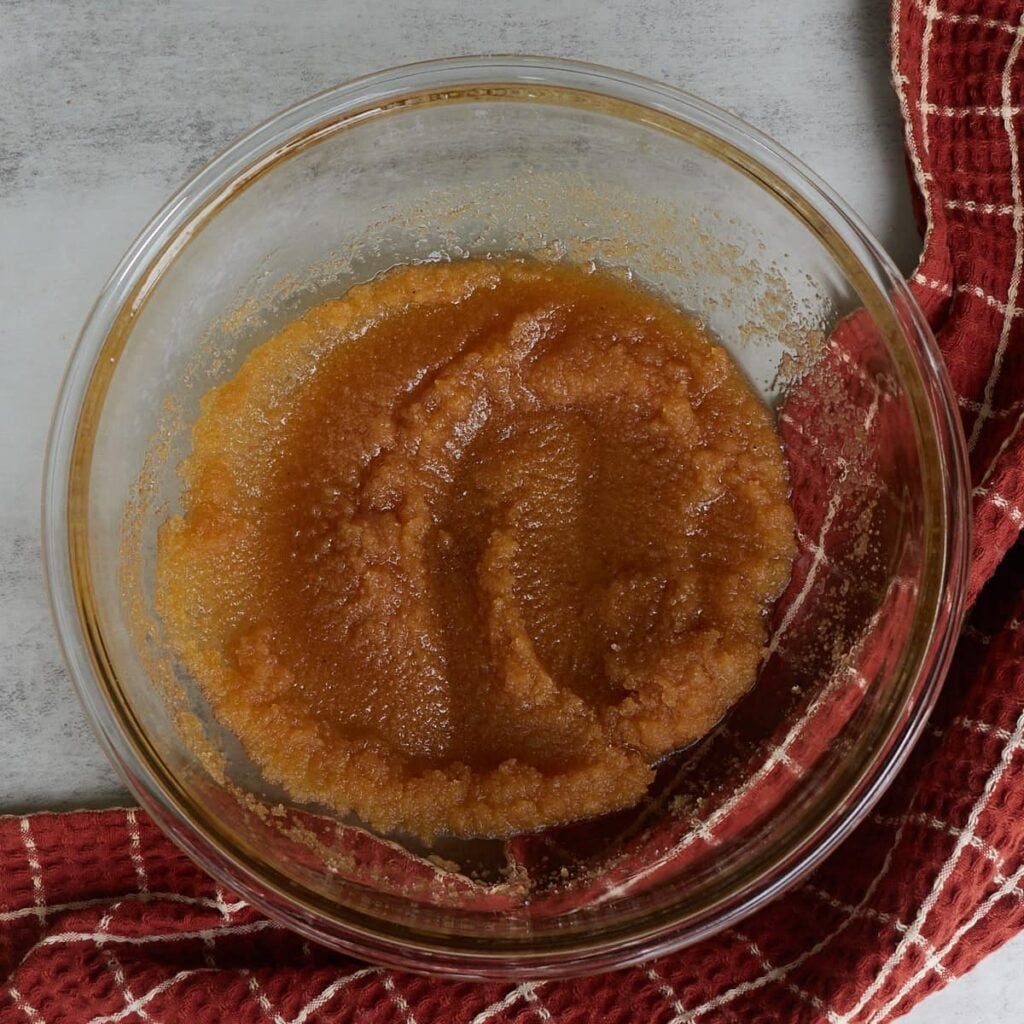 Brown butter, brown sugar, and granulated sugar mixed together in a glass bowl with a burnt orange and white checkered towel.