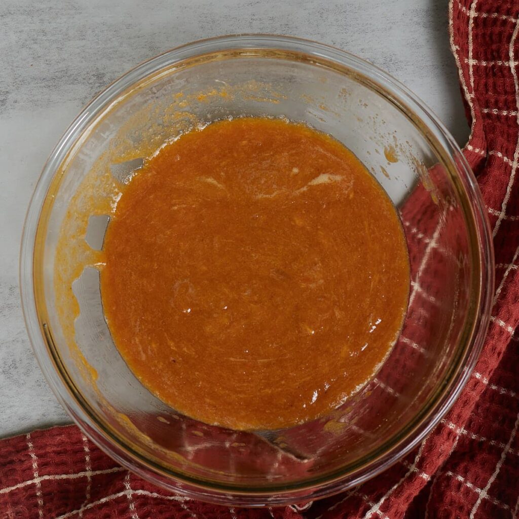 Wet ingredients for sourdough pumpkin cookie dough mixed together in a glass bowl with a burnt orange and white checkered towel.