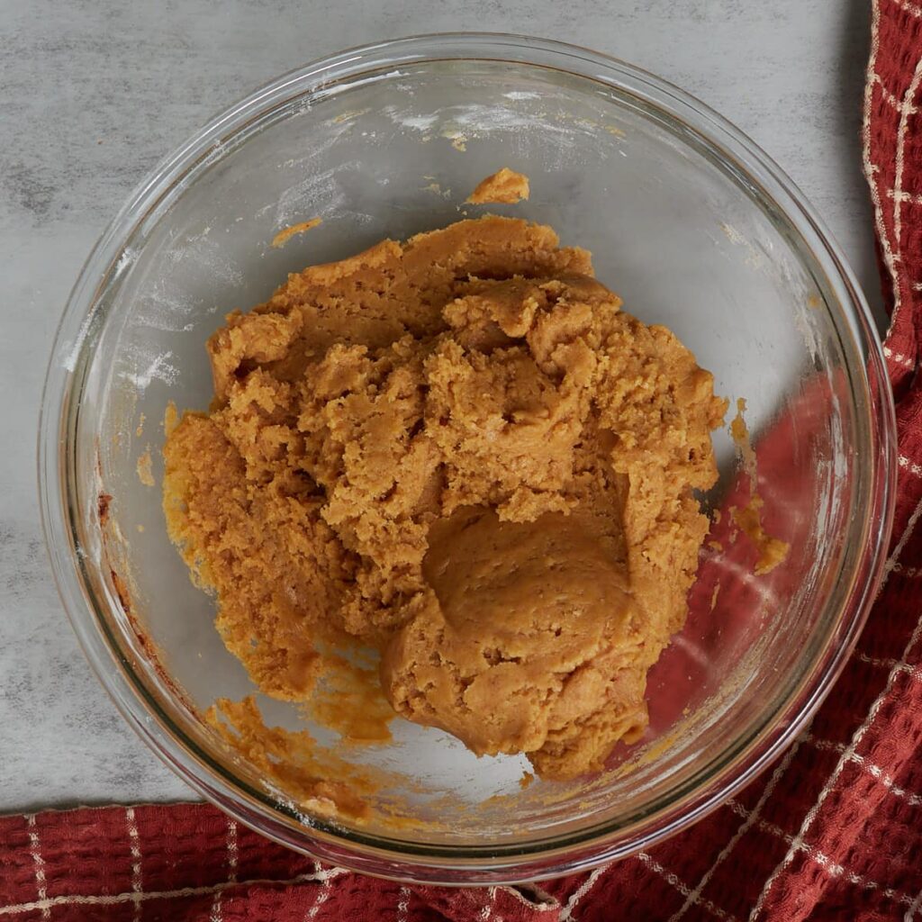 Sourdough pumpkin cookie dough mixed together in a glass bowl with a burnt orange and white checkered towel.