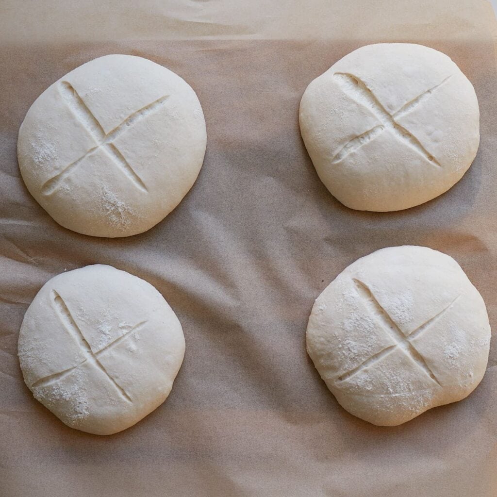 Sourdough bread bowl dough on parchment paper with an x scored on top.