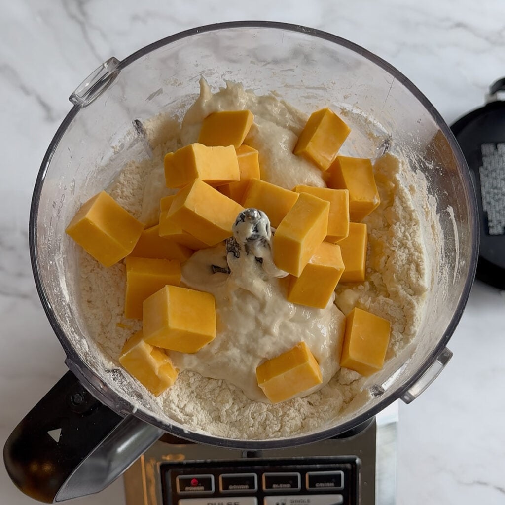 Milk, sourdough discard, and cubed cheddar cheese added to a food processor to make Sourdough Cheddar Biscuits.