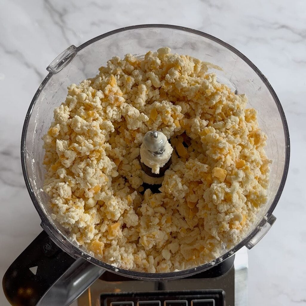 Sourdough Cheddar Biscuit dough in a food processor with the cheese, milk and sourdough discard added.