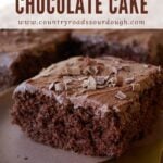 Slice of chocolate cake with chocolate butter cream frosting and chocolate shavings on a brown plate.