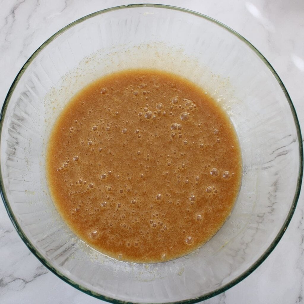 Oil, sugar, and eggs mixed together in a clear bowl for sourdough coffee cake.