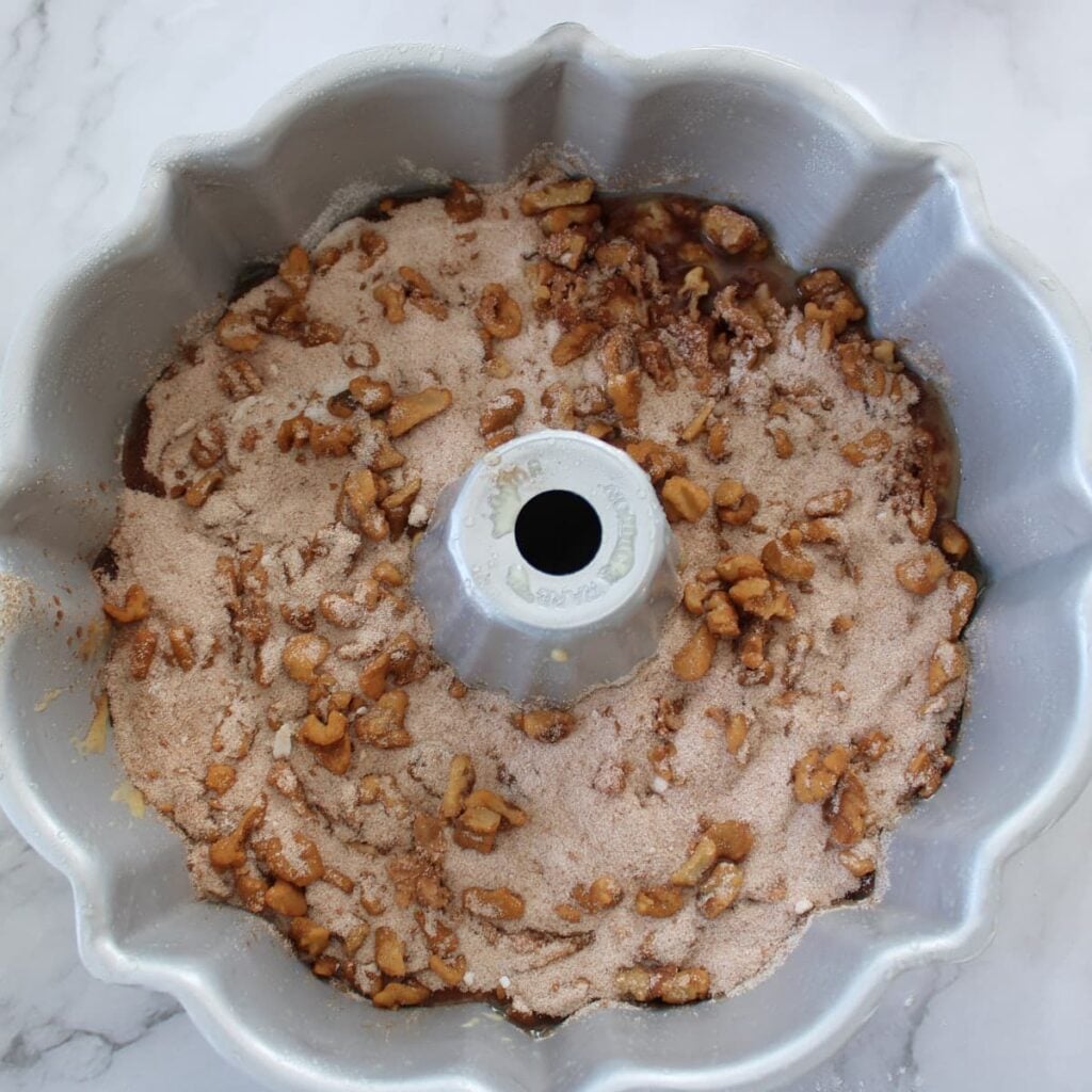Sourdough coffee cake batter in a bundt pan with a layer of cinnamon sugar and walnuts.