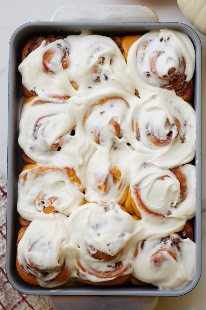 Sourdough pumpkin cinnamon rolls with cream cheese icing in a 9x13 pan.