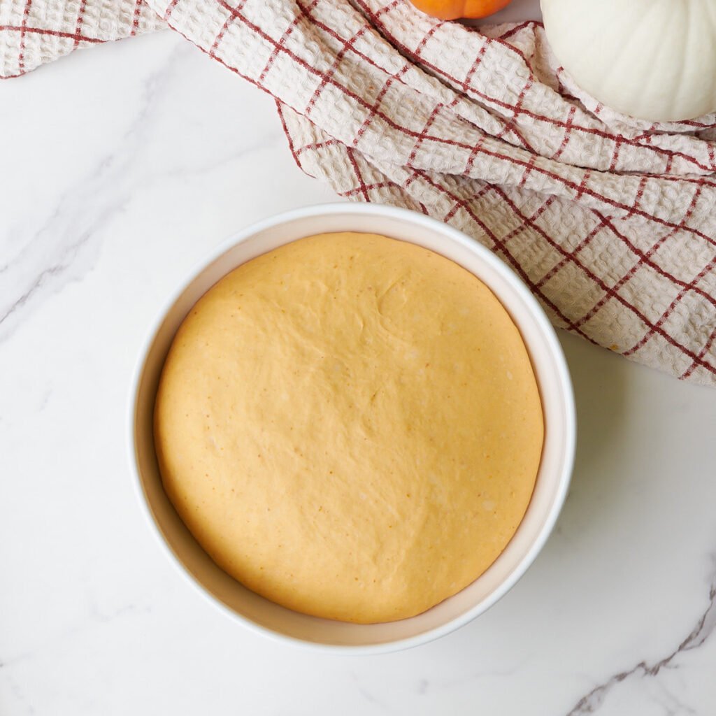 Sourdough pumpkin cinnamon roll dough in a white bowl after the first rise.
