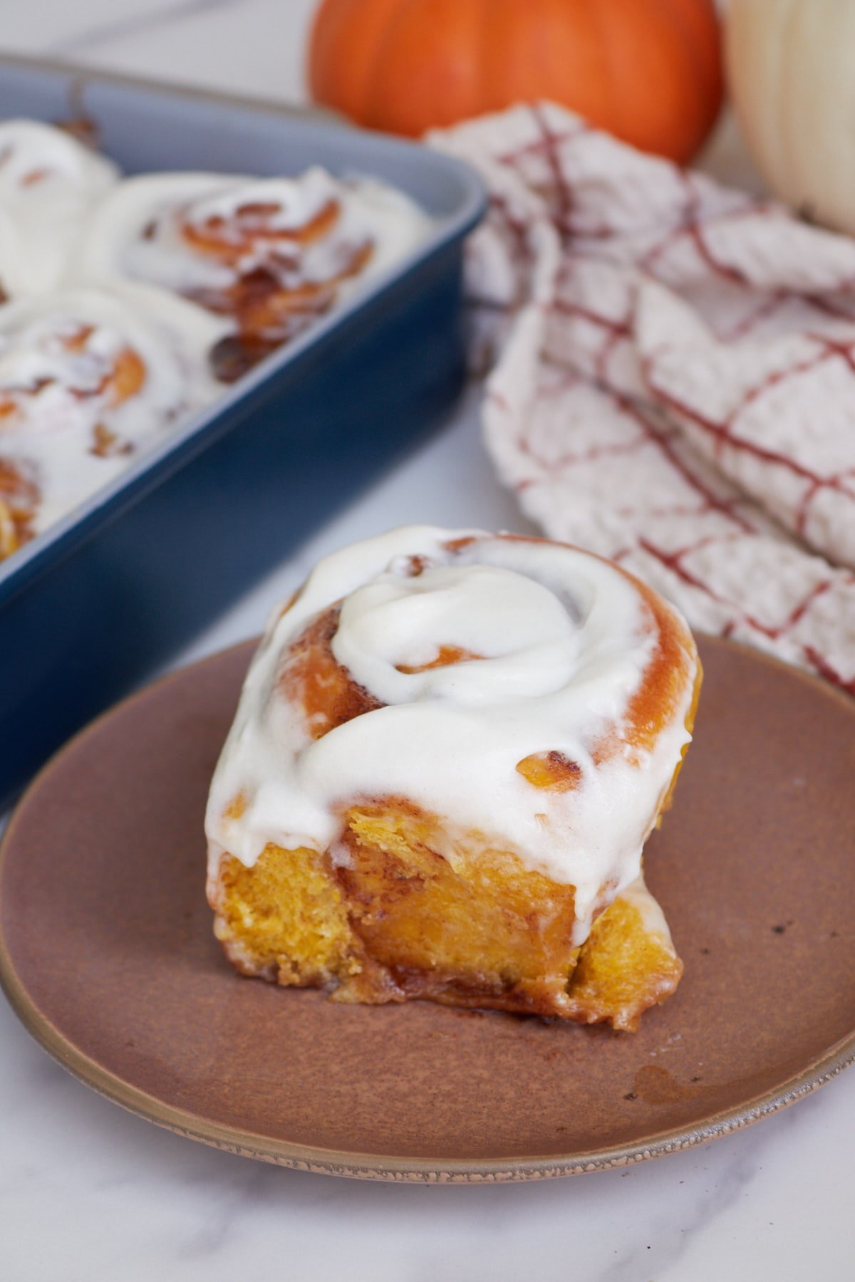 One Sourdough Pumpkin Cinnamon Rolls on a brown plate next to a 9x13 pan.